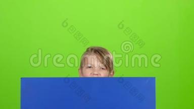 小男孩从<strong>蓝色海报</strong>后面看出来，在绿色屏幕前挥动一只手。 慢动作